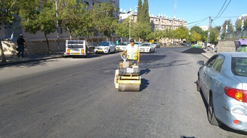 עובד אגף שפע מהדק עם מכבש את 'הפלסטר' לכביש